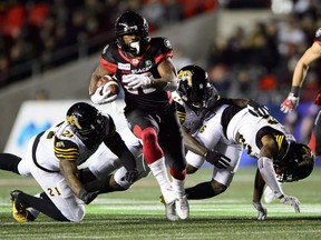Ottawa Redblacks running back William Powell (29) runs the ball as Hamilton Tiger-Cats linebacker Simoni Lawrence (21), left to right, Hamilton Tiger-Cats linebacker Larry Dean (11), and Hamilton Tiger-Cats defensive back Ethan Davis (26) attempt to tackle him during second half CFL action in Ottawa on Friday, Oct. 19, 2018.