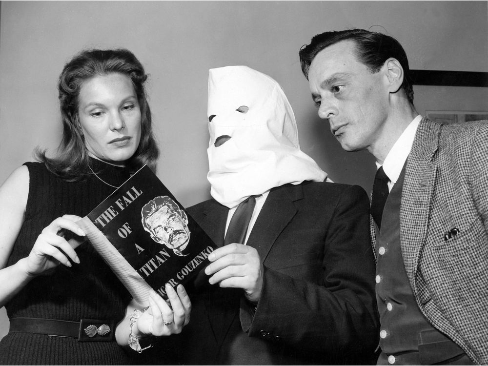 Igor Gouzenko, former Russian embassy code clerk in Ottawa whose disclosure led to cracking a Russian spy ring in Canada in 1946, poses with a pillow-case mask in a Toronto hotel room on April 11, 1954. Irja Jensen (left)  and Harry Towes will star in a film about the story. 