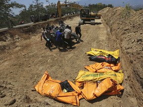 Indonesian police carry the body of a tsunami victim during a mass burial in Palu, Central Sulawesi, Indonesia, Monday, Oct. 1, 2018.