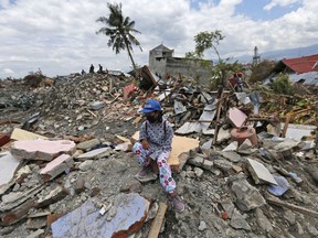 A woman sits on a pile of rubble in an area devastated by an earthquake in the Balaroa neighborhood of Palu, Central Sulawesi, Indonesia, Monday, Oct. 8, 2018. Aid has begun pouring into central Indonesia's Sulawesi island and humanitarian workers are fanning out across its countryside, more than a week after parts of the island were devastated by a powerful earthquake and tsunami.