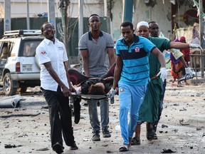 TOPSHOT - People rescue a wounded person following three blasts of suicide bomb car attacks in Mogadishu, on November 9, 2018. - At least 10 people were killed in blasts that occurred near a popular hotel and the police headquarters in the Somali capital Mogadishu, police said.