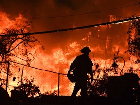 (FILES) In this file photo taken on November 9, 2018, a firefighter is silhouetted by a burning home along Pacific Coast Highway (Highway 1) during the Woolsey Fire in Malibu, California. - Climate change is already hurting the US and global economies and its effects will get worse unless more drastic action is taken to cut carbon emissions, a major US government report warned on Friday, November 23, 2018. "Without substantial and sustained global mitigation and regional adaptation efforts, climate change is expected to cause growing losses to American infrastructure and property and impede the rate of economic growth over this century," said the latest edition of the National Climate Assessment.