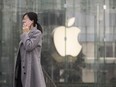 A woman uses a smartphone while walking past an Apple Inc. store in Shanghai, China.