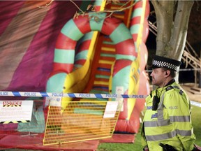 A police officer stands near an inflatable slide at a fireworks funfair in Woking Park, south England, Saturday Nov. 3, 2018.  British police say seven of the eight children hurt when they fell from an inflatable slide at a fair in southern England have been discharged from the hospital.