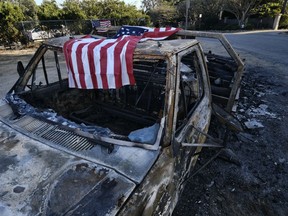 An American flag is draped over the charred remains of an old pickup truck entering Point Dume along the pacific coast highway in Malibu, Calif., on Sunday Nov. 11, 2018. Strong Santa Ana winds have returned to Southern California, fanning a huge wildfire that has scorched a string of communities west of Los Angeles. A one-day lull in the dry, northeasterly winds ended Sunday morning and authorities warn that the gusts will continue through Tuesday.