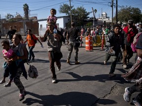 Migrants run toward the U.S. after breaking past a line of Mexican police at the Chaparral border crossing in Tijuana, Mexico, Sunday, Nov. 25, 2018, near the San Ysidro, California entry point.