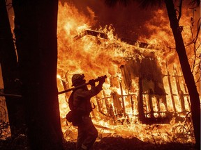 Firefighter Jose Corona sprays water as flames from the Camp Fire consume a home in Magalia, California.