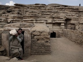 A worker carries an artifact out of a tomb, at an ancient necropolis near Egypt's famed pyramids in Saqqara, Giza, Egypt, Saturday, Nov. 10, 2018. A top Egyptian antiquities official says local archaeologists have discovered seven Pharaonic Age tombs near the capital Cairo containing dozens of cat mummies along with wooden statues depicting other animals.