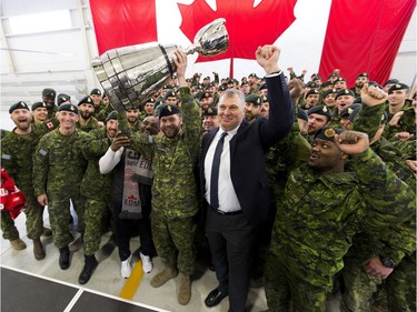 Cpl. Cody Williamson of Smithers, B.C., hoists the Grey Cup as he stands alongside CFL commissioner, Randy Ambrosie, right, and Edmonton Eskimos alumnus Henry "Gizmo" Williams, left, at Canadian Forces Base Edmonton on Tuesday.