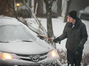 The predicted snow finally begins on Tuesday morning as Spencer Cuddington clears off the car in Nepean.