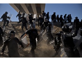 Mexican police run as they try to keep migrants from getting past the Chaparral border crossing in Tijuana, Mexico, Sunday, Nov. 25, 2018, near San Ysidro, California. The mayor of Tijuana has declared a humanitarian crisis in his border city and says that he has asked the United Nations for aid to deal with the approximately 5,000 Central American migrants who have arrived in the city.