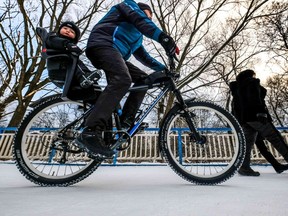 A father and his son ride a bicycle in a snow-covered park.