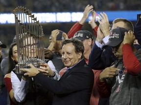 This Oct. 28, 2018, shows Boston Red Sox owner John Henry, partially hidden at left, and chairman Tom Werner holding the championship trophy beside manager Alex Cora, right, after Game 5 of baseball's World Series against the Los Angeles Dodgers in Los Angeles.