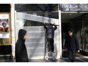 A man protects his shop a window on the Champs-Elysees avenue in Paris, Friday, Dec.14, 2018. Anticipating a fifth straight weekend of violent protests, Paris' police chief said Friday that armored vehicles and thousands of officers will be deployed again in the French capital this weekend.