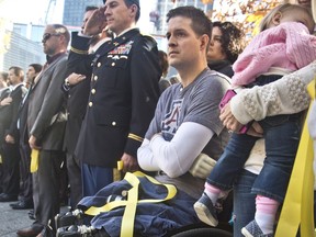 FILE--In this Nov. 10, 2014, file photo, former U.S. Air Force Senior Airman Brian Kolfage, center, sits in a wheelchair next to his wife Ashley, right, who holds their daughter Paris, during the National September 11 Memorial and Museum's "Salute to Service" tribute honoring U.S. veterans in New York. Kolfage, a triple-amputee who lost his limbs serving in Iraq in the U.S. Air Force, started a GoFundMe page to help fund construction of President Donald Trump's border wall has already raised millions of dollars.