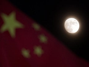 The moon is seen near a Chinese national flag in Beijing Sunday, Dec. 15, 2013.