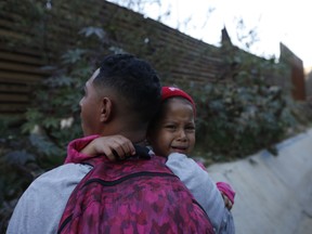 A Honduran migrant carries Jired Melendez, 4 years-old, as they try to cross over the U.S. border wall to San Diego, California, from Tijuana, Mexico, Saturday, Dec. 15, 2018.