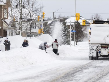 A snowplow clears Beatrice Drive as residents shovel out their driveway following a winter storm in Ottawa on February 13, 2019.