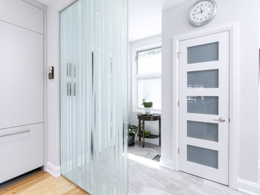 A custom frosted glass wall divides the kitchen from the front entry and newly added powder room creating a division between the competing spaces.