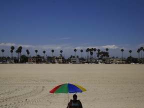 In a file photo, a beach-goer sits under an umbrella on the beach in Long Beach, Calif.
