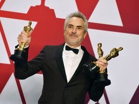 FILE - In this Sunday, Feb. 24, 2019, file photo, Alfonso Cuaron poses with the awards for best director for "Roma," best foreign language film for "Roma," and best cinematography for "Roma" in the press room at the Oscars at the Dolby Theatre in Los Angeles. "Roma" may not have won the best picture Oscar this year, but it came close enough to make some of Hollywood's top players worry about Netflix's infiltration of their most prestigious award.