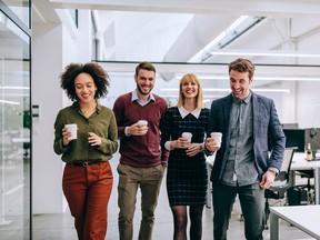 Group of diverse coworkers walking through a corridor in an office, holding paper cups