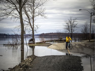 The Ottawa River has flooded the many parts of the road. A cyclist stops at the edge of a flooded area.