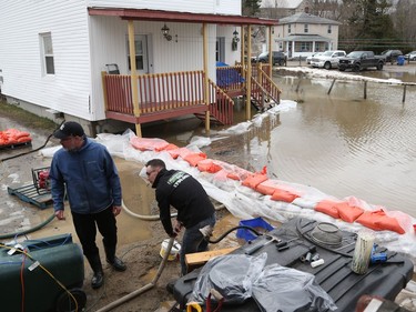 Jacob Boucher-Pilon (right) and Eric Thérrien work on their pumps as homes and streets of Saint-André-Avellin are flooded by the the Petite-Nation River on Wednesday.