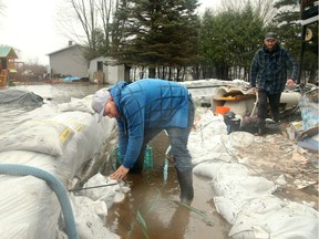 Kris Blais, left, has been working around the clock since last week, running four pumps and building walls of sandbags around his sister and brother-in-law Dave Proulx's (right) home in Masson-Angers.