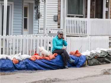Julie Lafayette and her dog "Mademoiselle" sit on sand bags guarding her rue Moreau home from flood waters in Gatineau, Quebec on April 23, 2019.