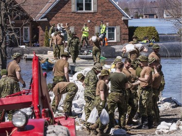 Members of the Canadian Armed Forces move sandbags to  combat flood waters along Leo Lane in Cumberland on Sunday.