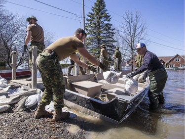 Ian Charebois (R) uses a small boat to pick up sandbags from members of the Canadian Armed Forces combat flood waters at a colleagues home along Leo Lane in Cumberland on Sunday.
