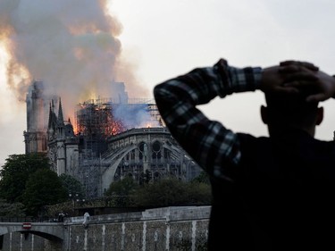 TOPSHOT - A man watches the landmark Notre-Dame Cathedral burn, engulfed in flames, in central Paris on April 15, 2019. - A huge fire swept through the roof of the famed Notre-Dame Cathedral in central Paris on April 15, 2019, sending flames and huge clouds of grey smoke billowing into the sky. The flames and smoke plumed from the spire and roof of the gothic cathedral, visited by millions of people a year. A spokesman for the cathedral told AFP that the wooden structure supporting the roof was being gutted by the blaze.