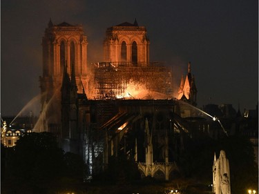 Firefighter douse flames billowing from the roof at Notre-Dame Cathedral in Paris on April 15, 2019. - A major fire broke out at the landmark Notre-Dame Cathedral in central Paris sending flames and huge clouds of grey smoke billowing into the sky, the fire service said. The flames and smoke plumed from the spire and roof of the gothic cathedral, visited by millions of people a year, where renovations are currently underway.