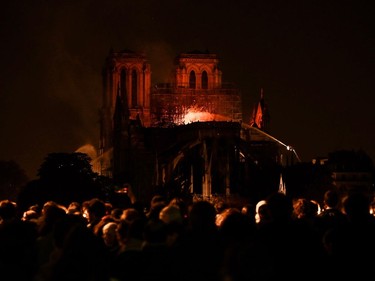 Bystanders look on as flames and smoke billow from the roof at Notre-Dame Cathedral in Paris on April 15, 2019. - A major fire broke out at the landmark Notre-Dame Cathedral in central Paris sending flames and huge clouds of grey smoke billowing into the sky, the fire service said. The flames and smoke plumed from the spire and roof of the gothic cathedral, visited by millions of people a year, where renovations are currently underway.