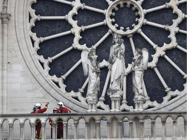 Firefighters talk near the rose window of Notre Dame cathedral Tuesday April 16, 2019 in Paris. Experts assessed the blackened shell of Paris' iconic Notre Dame Tuesday morning to establish next steps to save what remains after a devastating fire destroyed much of the cathedral that had survived almost 900 years of history.