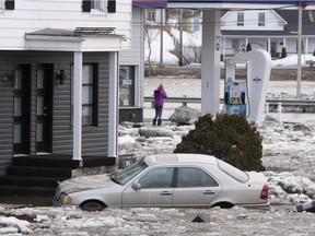 A woman looks at the Chaudière River as a flooded car sits in the foreground, Tuesday, April 16, 2019 in Beauceville Quebec. The floods forced the evacuation of 230 buildings and 36 people.
