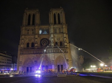 Firefighters spray water onto the facade of Notre Dame cathedral to stop the spread of a fire in Paris, Monday, April 15, 2019. Massive plumes of yellow brown smoke is filling the air above Notre Dame Cathedral and ash is falling on tourists and others around the island that marks the center of Paris.