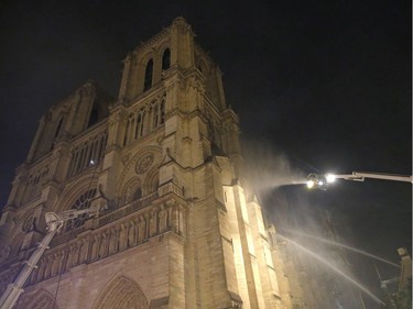 Firefighters spray water onto the facade of Notre Dame cathedral to stop the spread of a fire in Paris, Monday, April 15, 2019. Massive plumes of yellow brown smoke is filling the air above Notre Dame Cathedral and ash is falling on tourists and others around the island that marks the center of Paris.