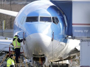 FILE- In this March 13, 2019, file photo a worker stands on a platform near a Boeing 737 MAX 8 airplane being built for TUI Group at Boeing Co.'s Renton Assembly Plant in Renton, Wash. Boeing is cutting production of its grounded Max airliner this month to focus on fixing flight-control software and getting the planes back in the air. The company said Friday, April 5, that starting in mid-April it will cut production of the 737 Max from 52 to 42 planes per month.