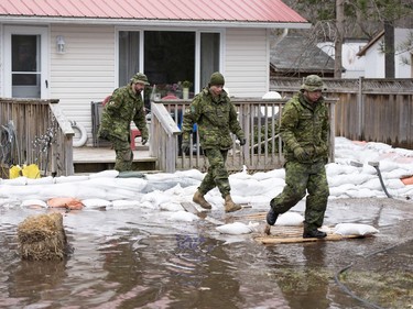 Canadian Forces members use a pallets as a makeshift walkway to access a home surrounded by water in the Ottawa community of Constance Bay as flooding continues to affect the region, on Saturday, April 27, 2019.