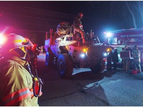 First responders look on as a Canadian Forces armoured vehicle drives on a road towards the flood zone in Ste-Marthe-sur-le-Lac, Que., on Saturday, April 27, 2019. The road has been blocked due to a broken dike which has prompted officials to evacuate hundreds of people in the area.