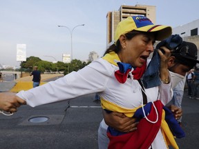 A woman suffocated by tear gas is aided by fellow opponents of President Nicolas Maduro outside La Carlota air base in Caracas, Venezuela, Tuesday, April 30, 2019.