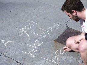 Avid cyclist Scott Conrad draws a message in chalk on the sidewalk of Laurier Avenue in Ottawa where a man riding a bike was killed by a hit-and-run driver on May 16, 2019.