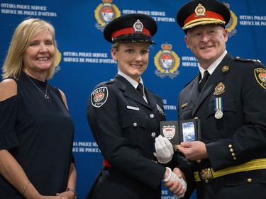 Amber Chouinard (centre) is presented her badge by Interim Police Chief Steven Bell (right) with Diane Deans, Chair of the Ottawa Police Services Board (left) as 88 Ottawa Police Service recruits received their police badges as part of the graduating ceremony held at the EY Centre.
