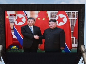 News footage of Chinese President Xi Jinping (L) being greeted in Pyongyang by North Korean leader Kim Jong Un is shown on a large screen outside a shopping mall in Beijing on June 20, 2019.