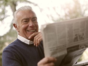 File: An older man smiling and reading the newspaper.