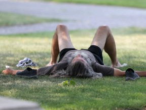A man with long grey hair and a large beard relaxes in the shade in Memorial Park, during a heat wave in Winnipeg in August 2018.