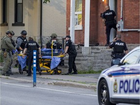 Members of the Ottawa Police Service Tactical Unit and tactical paramedics with other officers assist in transporting an unidentified man to a waiting ambulance at a crime scene on Lyon Street on Friday evening.