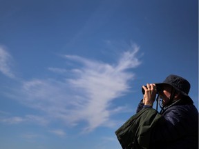 A member of the Cloud Appreciation Society, pictured against Cirrus clouds, looks through binoculars during a boat trip around Lundy, Britain, May 21, 2019. Picture taken May 21, 2019.